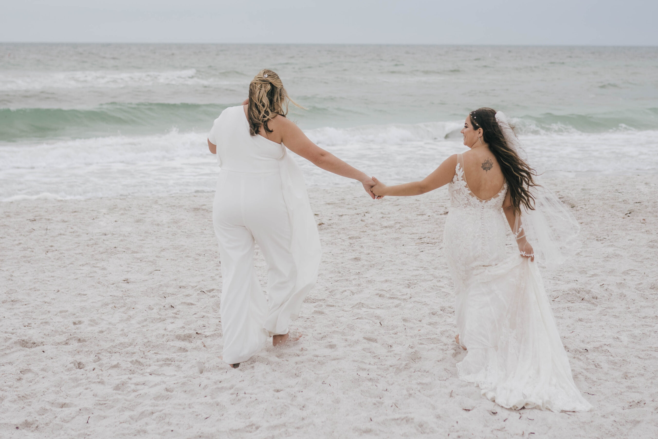 two brides holding hands on the beach